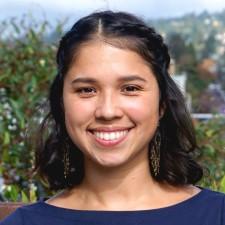 Xenia Mendez headshot. Woman with brown hair in front of a nature background. 